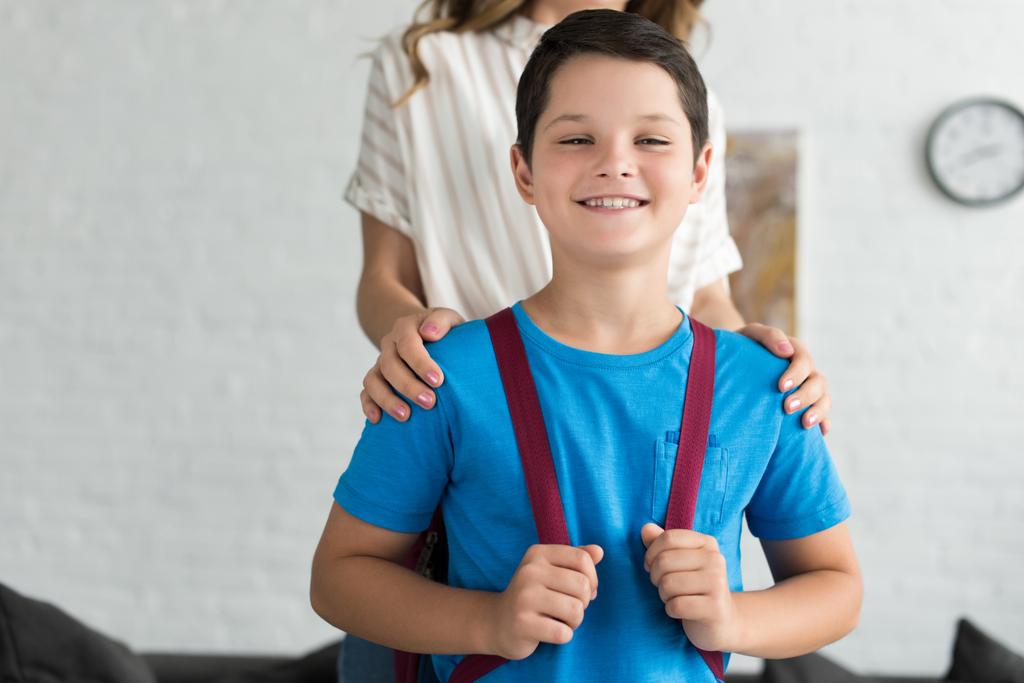Teilansicht von Mutter und lächelndem Jungen mit Rucksack zu Hause, zurück zum Schulkonzept - Foto, Bild