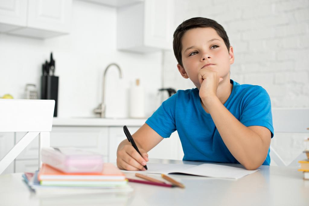портрет вдумчивого мальчика, делающего домашнее задание в одиночестве за столом дома
 - Фото, изображение
