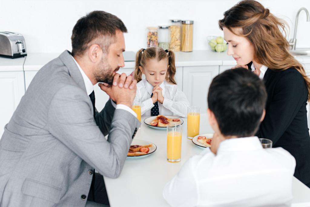 familie bidden aan tafel tijdens het ontbijt in de keuken thuis - Foto, afbeelding