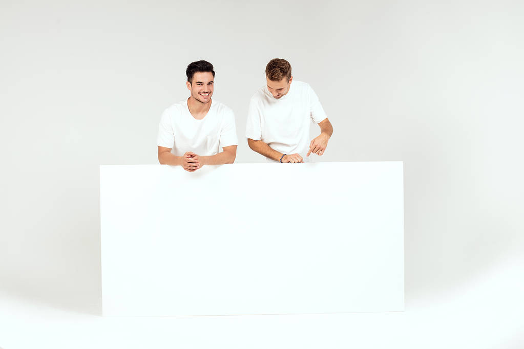 Two young handsome guys holding blank white banner, signboard, isolated on white studio background. - Photo, Image