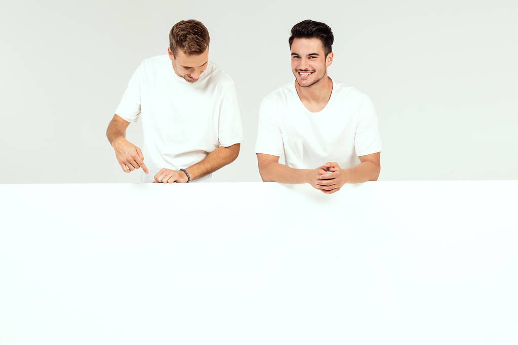 Due giovani bei ragazzi in possesso di banner bianco vuoto, cartello, isolato su sfondo bianco studio
. - Foto, immagini