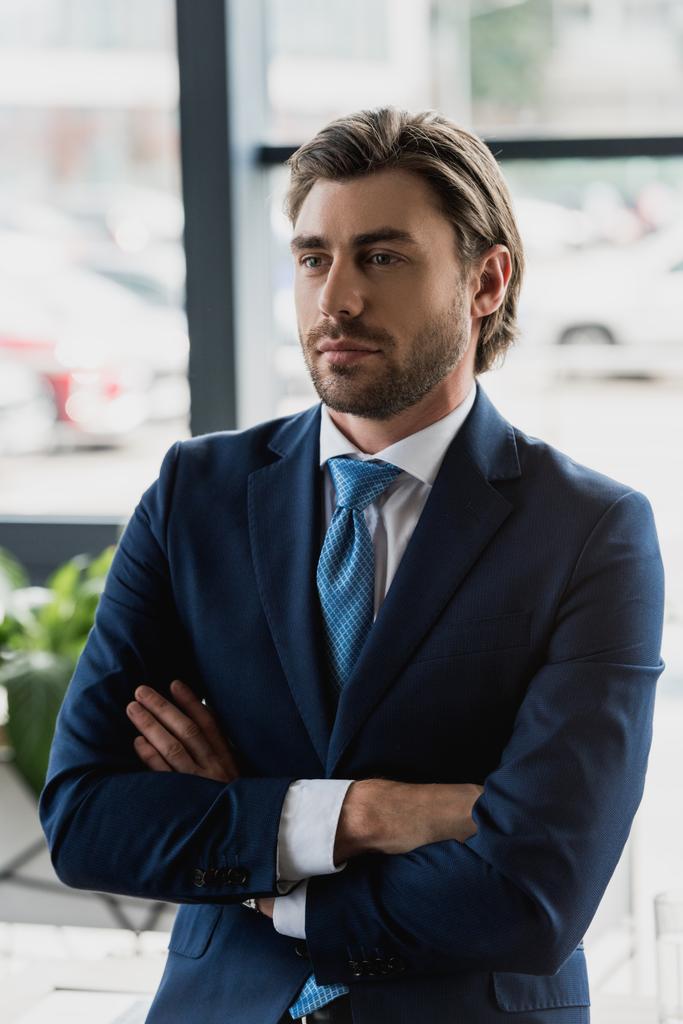 handsome young bearded businessman in suit standing with crossed arms and looking away - Photo, Image