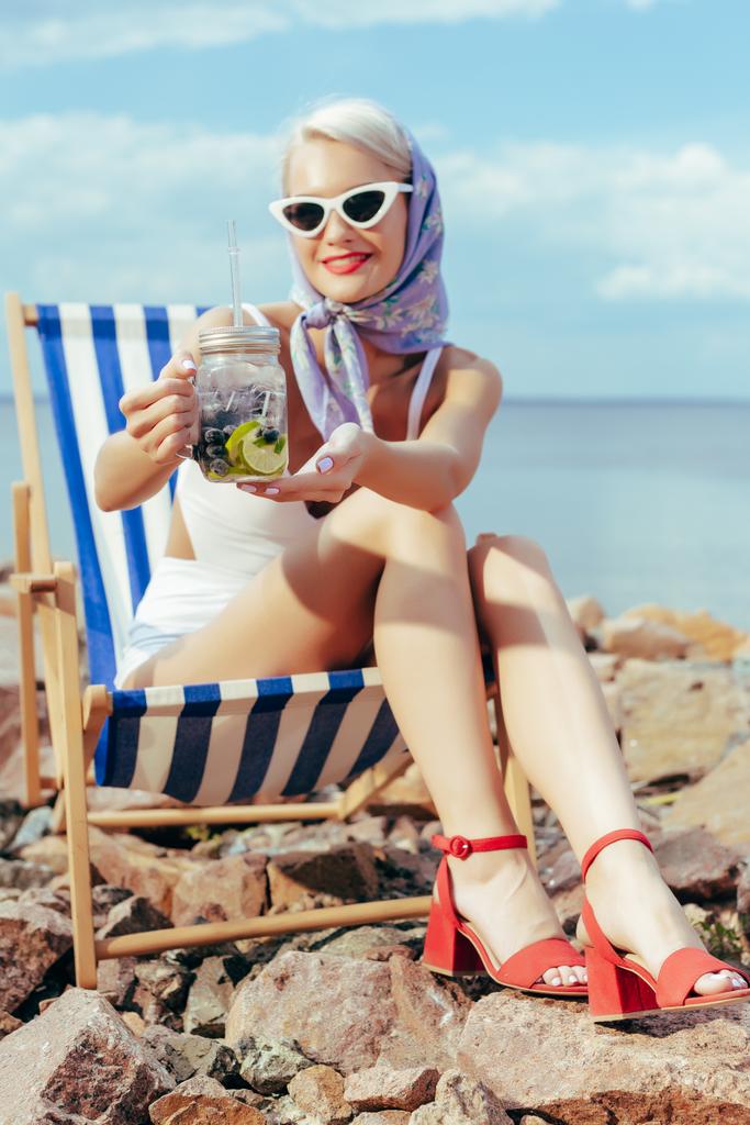 schönes lächelndes Mädchen, das Limonade im Einmachglas hält und sich im Strandkorb ausruht - Foto, Bild