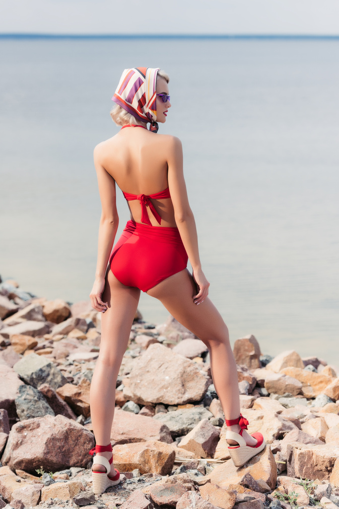 vista trasera de la chica elegante posando en bikini rojo en la playa rocosa
 - Foto, imagen