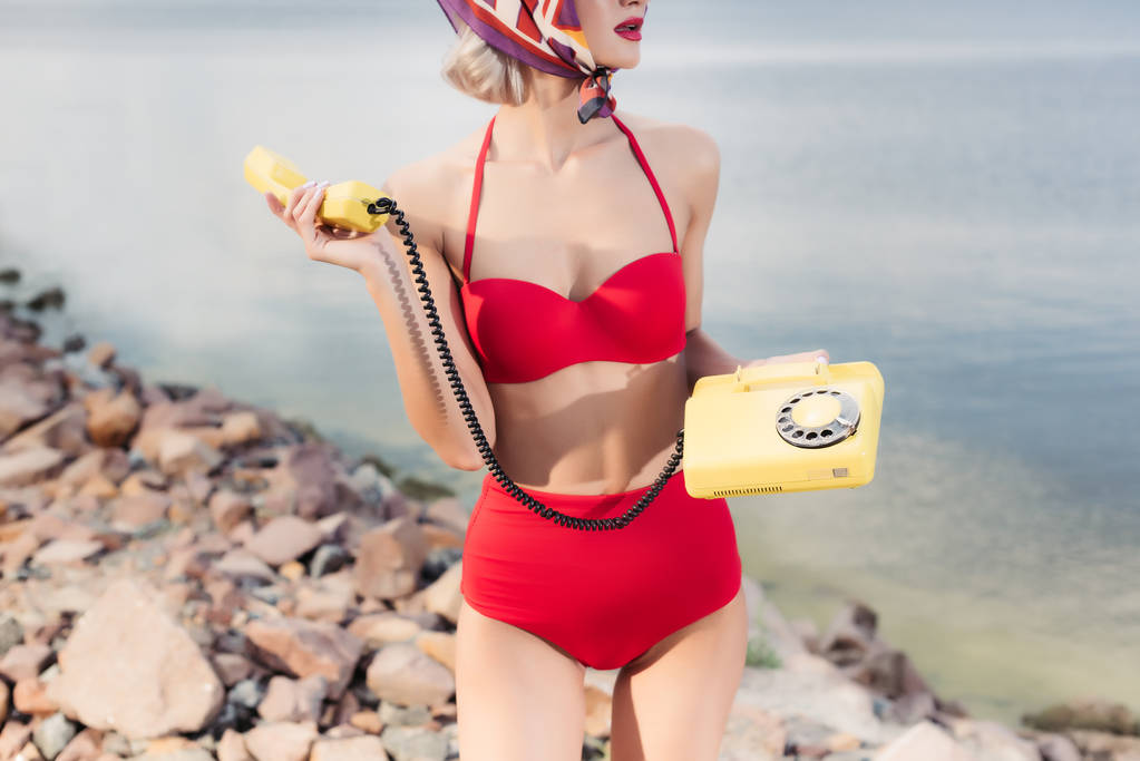 vue recadrée de la fille en bikini rouge posant avec téléphone rotatif sur la plage rocheuse
 - Photo, image