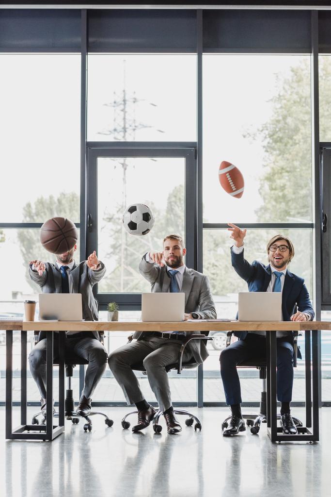 nuoret liikemiehet heittää palloa työskennellessään kannettavat toimistossa
   - Valokuva, kuva