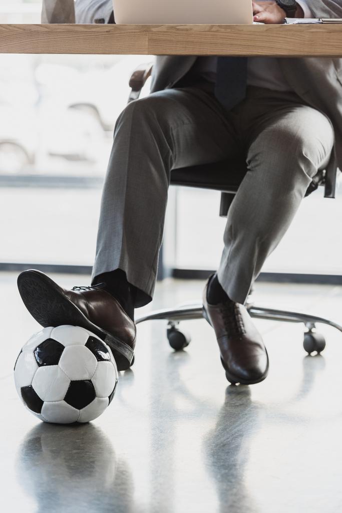 обрезанный снимок молодого бизнесмена с футбольным мячом с помощью ноутбука в офисе
  - Фото, изображение