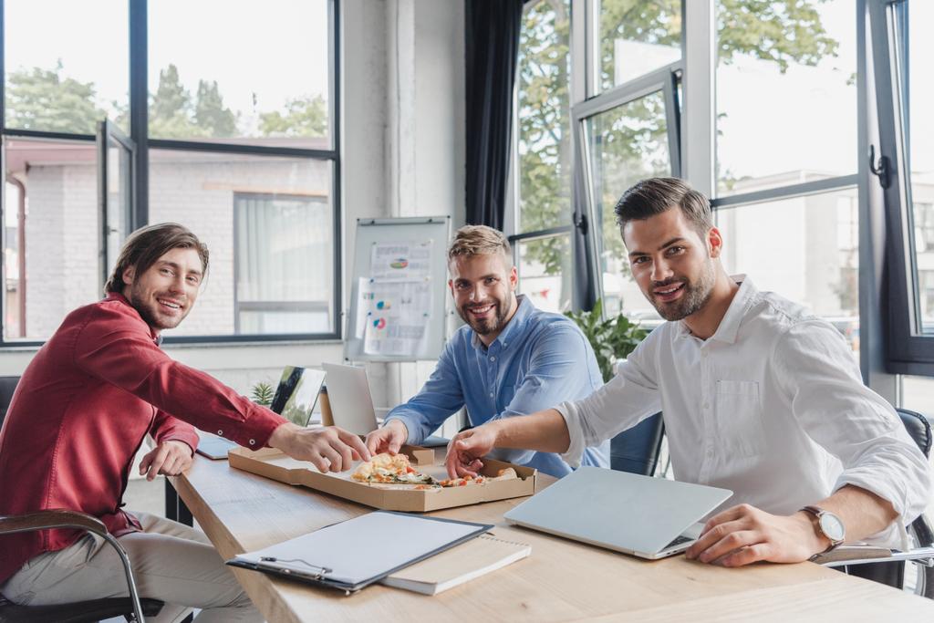 jonge ondernemers eten van pizza en lachend op camera in kantoor - Foto, afbeelding