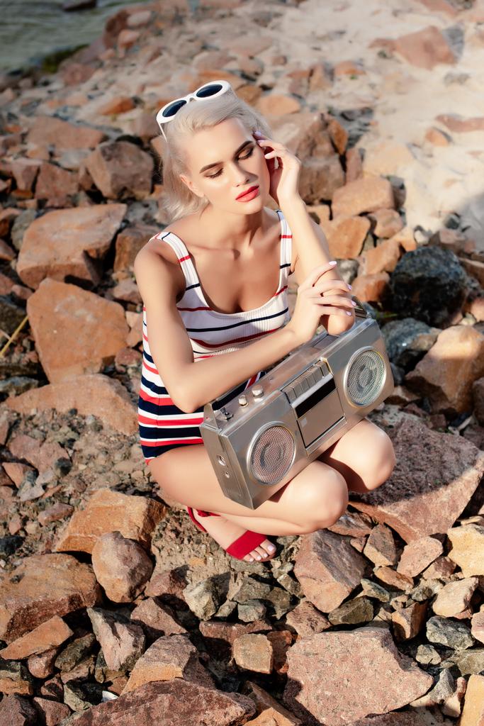 Blonde Frau im Badeanzug posiert mit Vintage-Kassettenrekorder auf Felsen - Foto, Bild