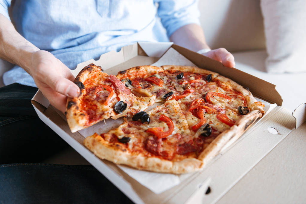 Close up of a pizza in box on men's lap on a couch - Photo, Image