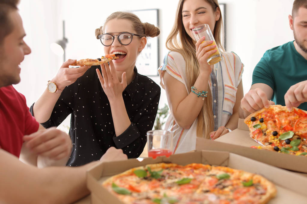 Νέοι διασκεδάζουν πάρτι με νόστιμη πίτσα σε εσωτερικούς χώρους - Φωτογραφία, εικόνα