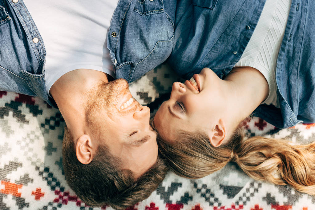 Draufsicht auf lächelndes junges Paar, das auf gemustertem Tuch liegt - Foto, Bild