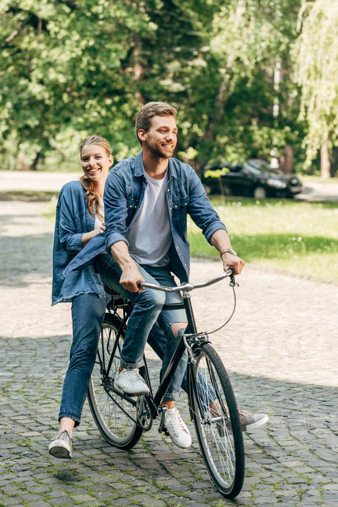 Happy νεαρό ζευγάρι ιππασία ποδήλατο μαζί στο πάρκο - Φωτογραφία, εικόνα