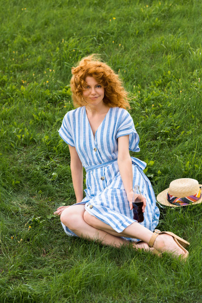 soda ile çimenlerin üzerinde oturan çekici Kızıl saçlı kadın  - Fotoğraf, Görsel
