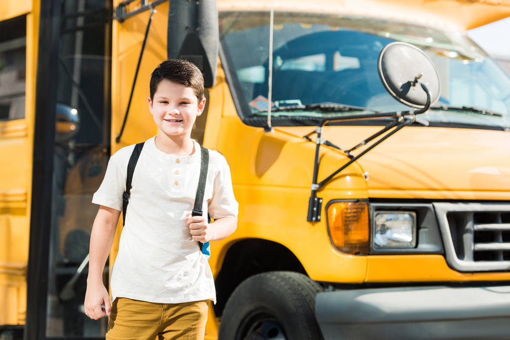 sırt çantası ayakta önünde okul otobüsü ile mutlu küçük öğrenci - Fotoğraf, Görsel