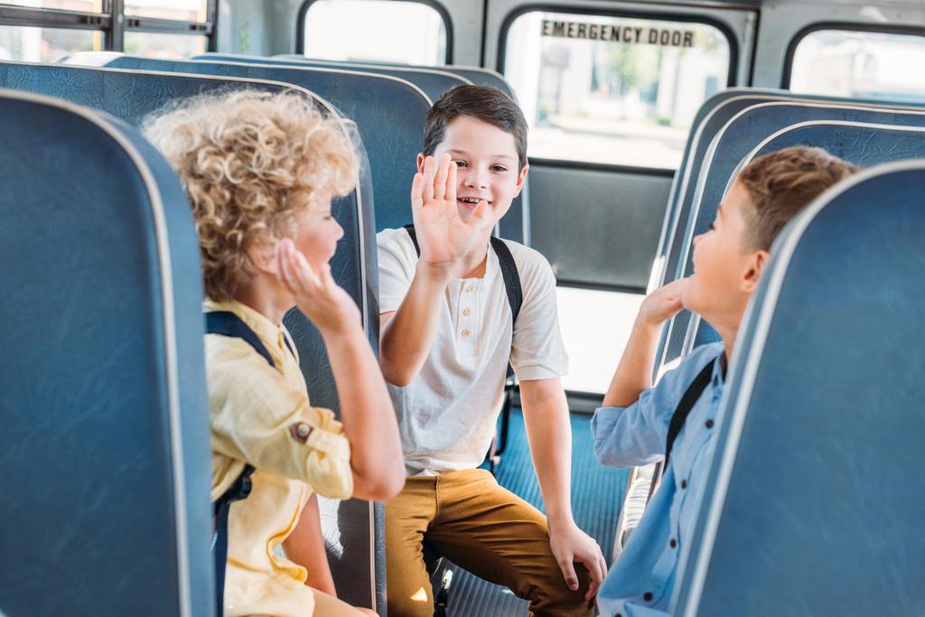 группа очаровательных учеников, дающих пять вместе во время езды на школьном автобусе
 - Фото, изображение