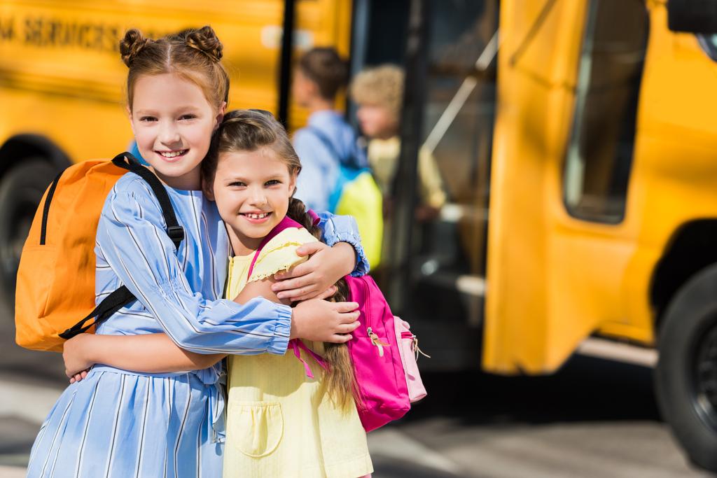 szép boldog iskolás látszó-on fényképezőgép és a átfogó előtt iskolabusz - Fotó, kép
