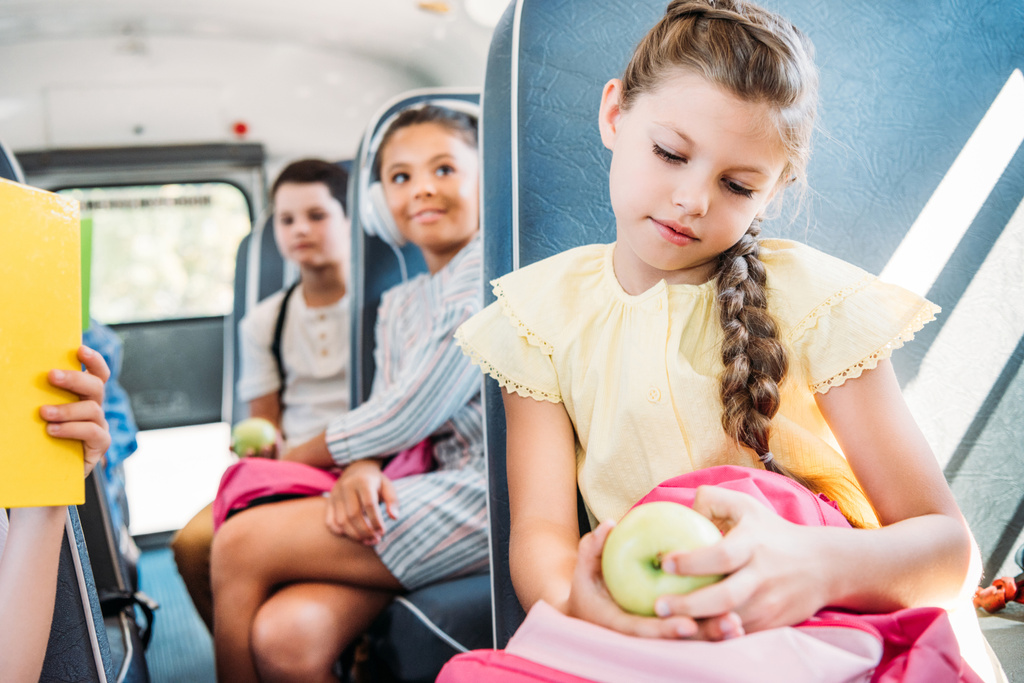 hermosa colegiala con mochila y manzana a caballo en el autobús escolar con compañeros de clase borrosa en el fondo
 - Foto, Imagen