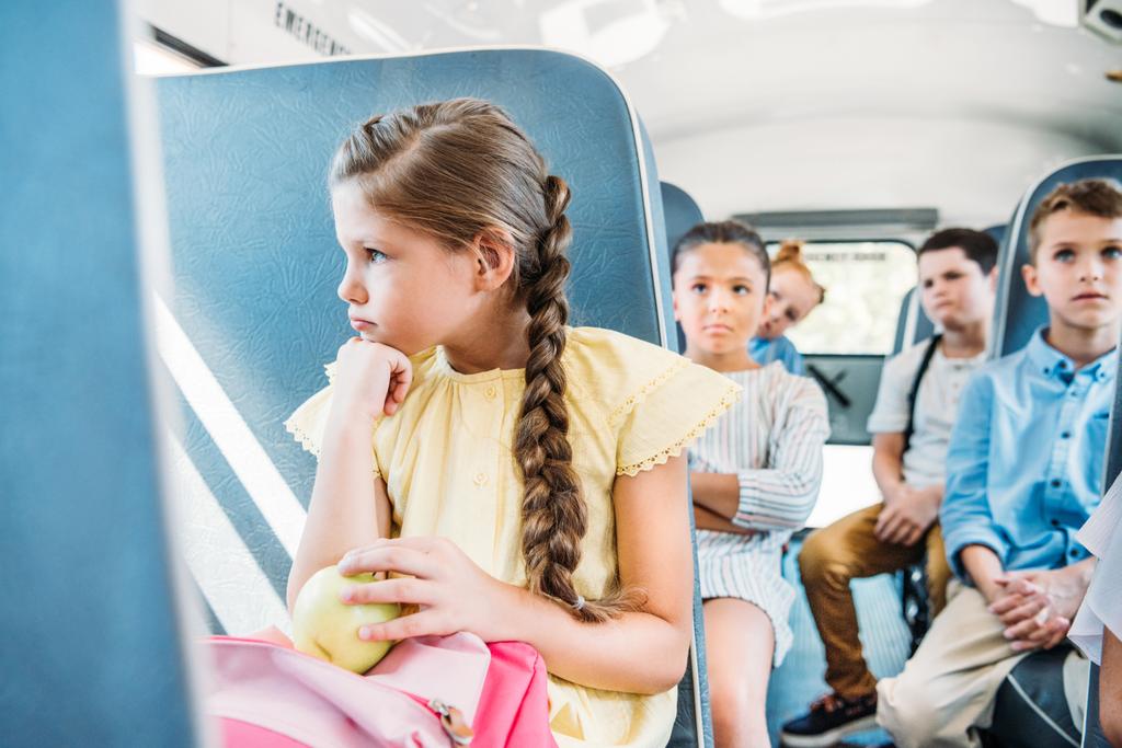 triest weinig schoolmeisje rijden op schoolbus met haar klasgenoten - Foto, afbeelding