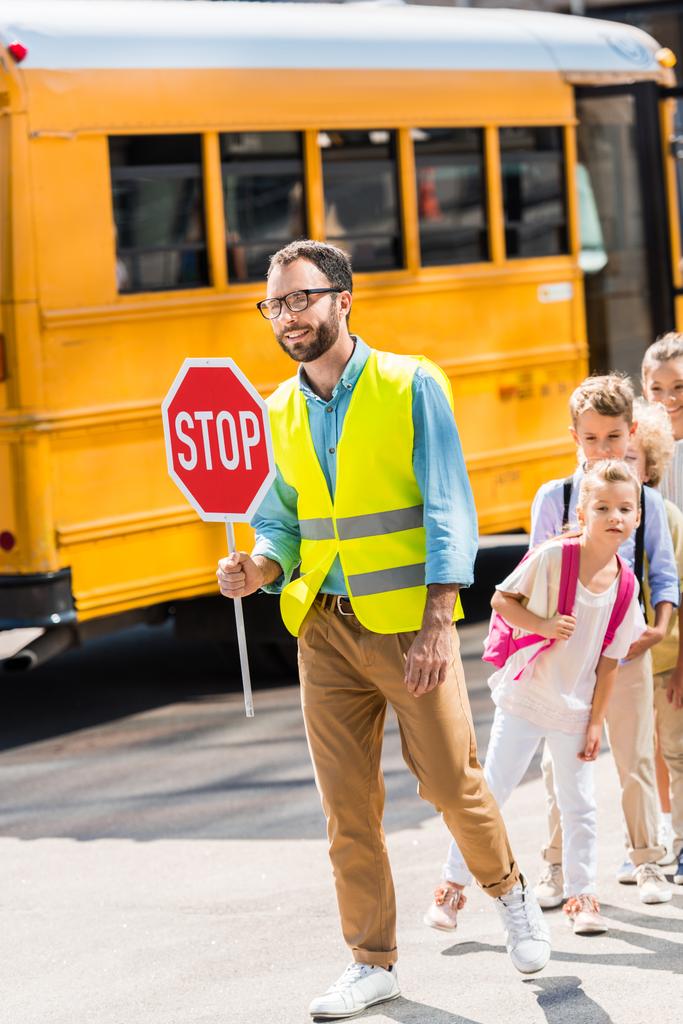 ευτυχισμένος φρουρά διέλευση οδική κυκλοφορία με τους μαθητές μπροστά σε σχολικό λεωφορείο - Φωτογραφία, εικόνα