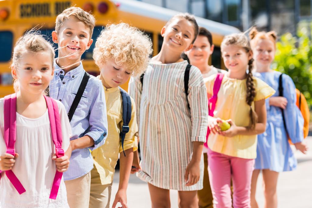 группа счастливых учеников, стоящих в ряд перед школьным автобусом
 - Фото, изображение