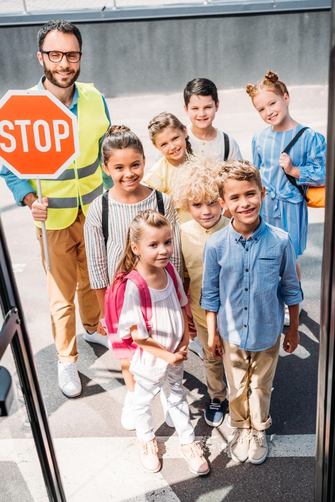 view from school bus at group of schoolchildren with traffic guard looking at camera - Photo, Image