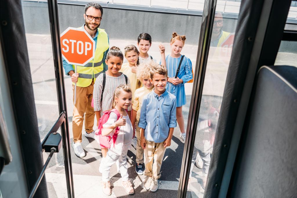 vista de ônibus escolar em grupo de estudiosos felizes com guarda de tráfego olhando para a câmera
 - Foto, Imagem