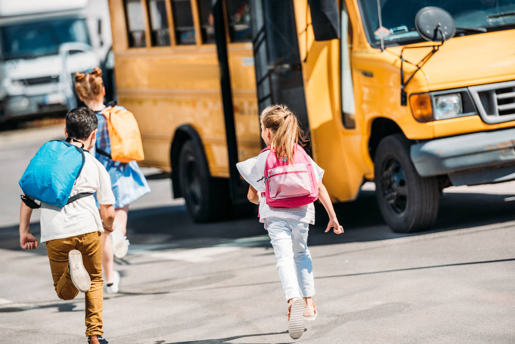 Rückansicht entzückender Schulkinder, die zum Schulbus rennen - Foto, Bild