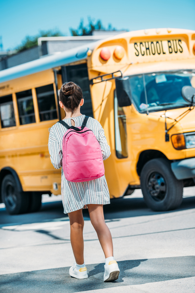 вид сзади школьницы с рюкзаком, стоящей перед школьным автобусом
 - Фото, изображение