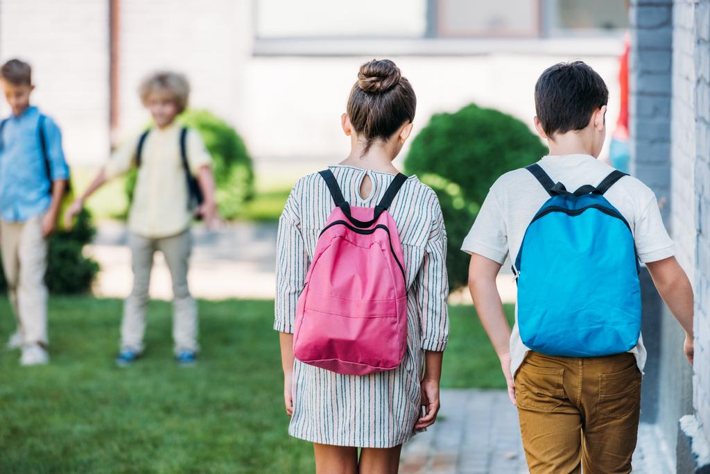 Achteraanzicht van schoolkinderen met bakpacks spoorfietsen door schooltuin - Foto, afbeelding