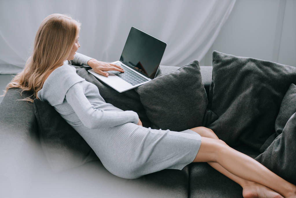 mujer embarazada usando el ordenador portátil con pantalla en blanco en el sofá en casa
 - Foto, Imagen