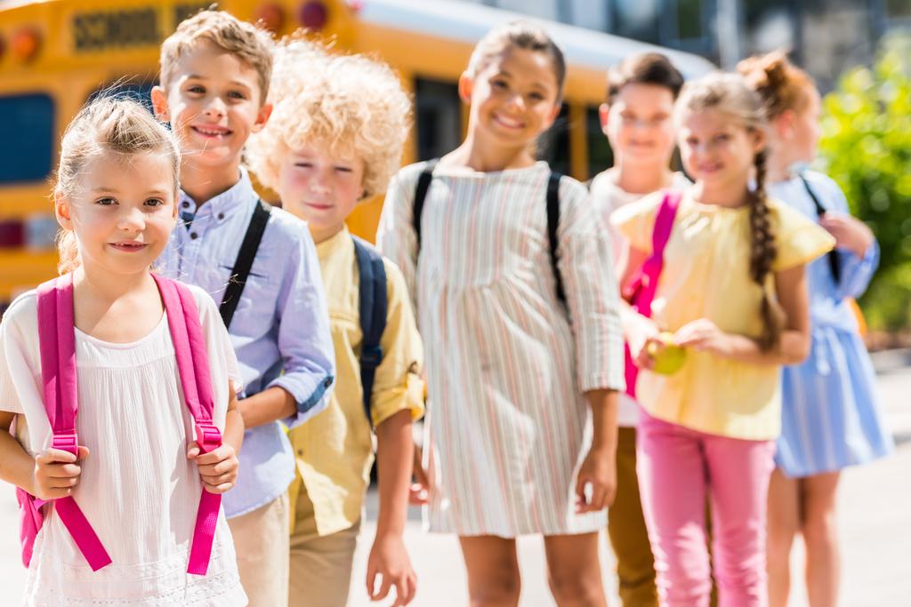 група чарівних школярів, що стоять поспіль перед шкільним автобусом і дивляться на камеру
 - Фото, зображення