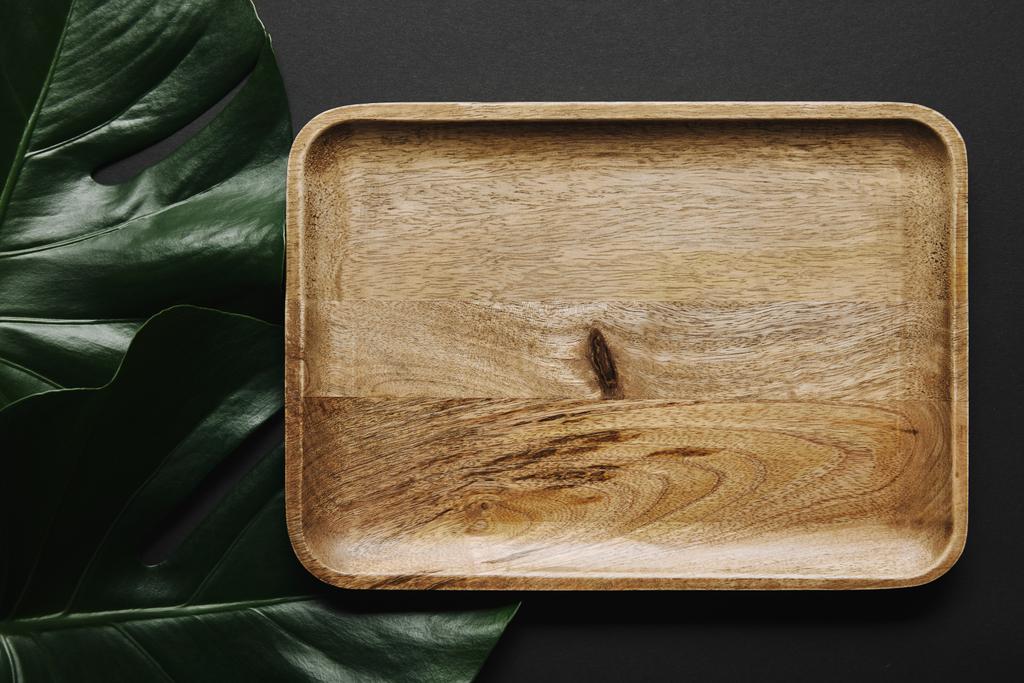 Empty wooden board on black background with monstera leaves - Photo, Image