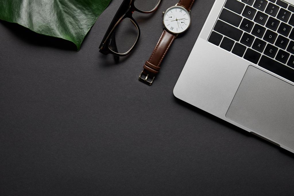 Bril en horloge door laptop op zwarte achtergrond - Foto, afbeelding