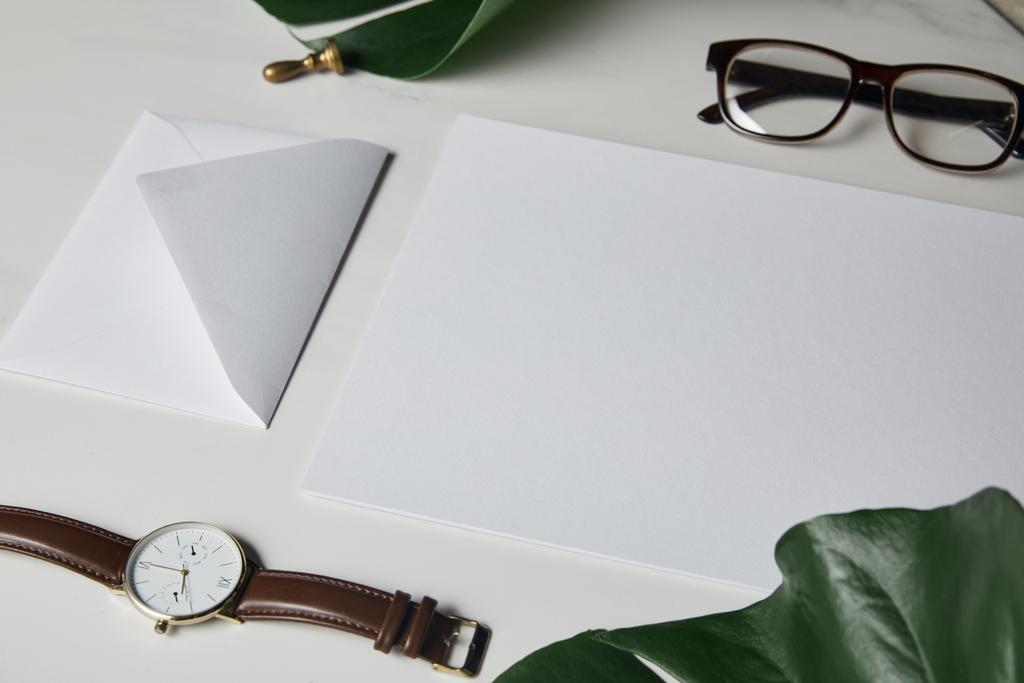 Briefsjabloon met bril en horloge op witte marmeren achtergrond met monstera verlaat - Foto, afbeelding