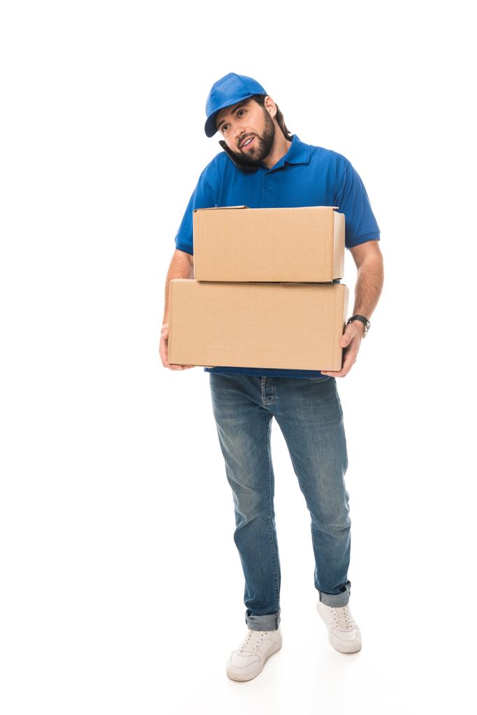 молодий чоловік доставки тримає картонні коробки і розмовляє по смартфону ізольовано на білому
 - Фото, зображення