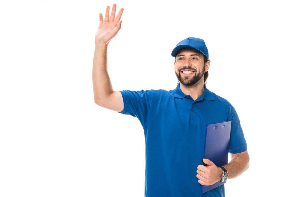 happy young delivery man holding clipboard and waving hand isolated on white  - Photo, Image
