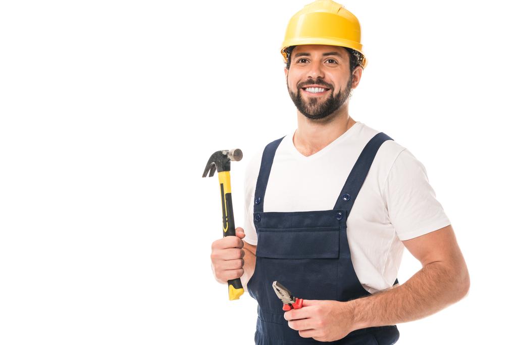 красивый улыбающийся рабочий держит плоскогубцы и молоток изолированы на белом
 - Фото, изображение
