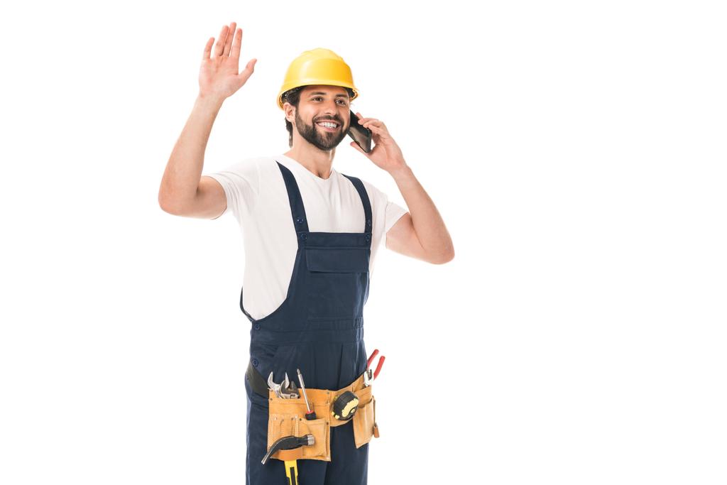 Fröhlicher Bauarbeiter spricht per Smartphone und winkt mit weißer Hand - Foto, Bild
