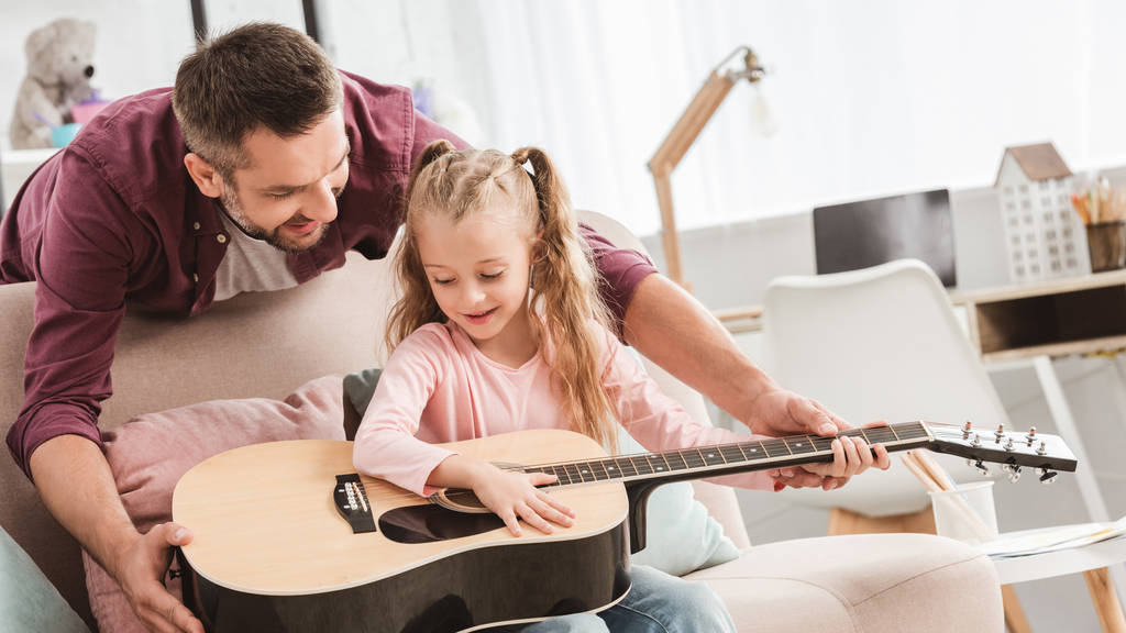 отец и улыбающаяся дочь играют дома на гитаре
 - Фото, изображение