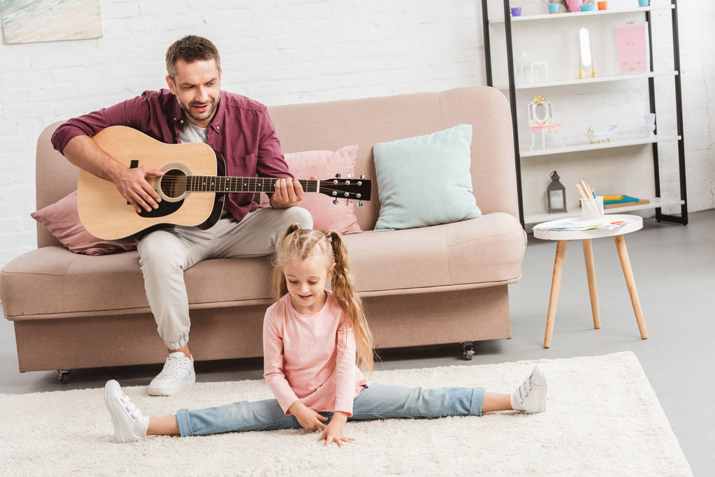 heerful Tata gra na gitarze, podczas gdy córka robi podzielone na piętrze - Zdjęcie, obraz
