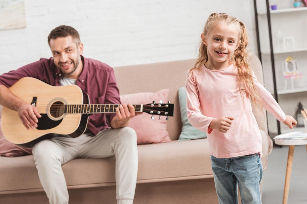 happy daughter dancing while father playing on guitar - Photo, Image