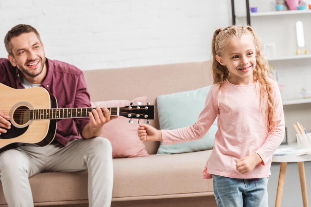 happy daughter dancing while father playing on guitar - Photo, Image