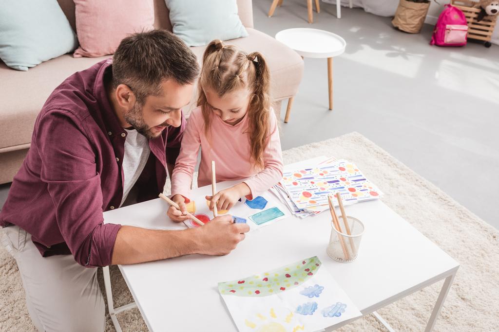Отец и дочь веселятся и рисуют на белом столе
 - Фото, изображение