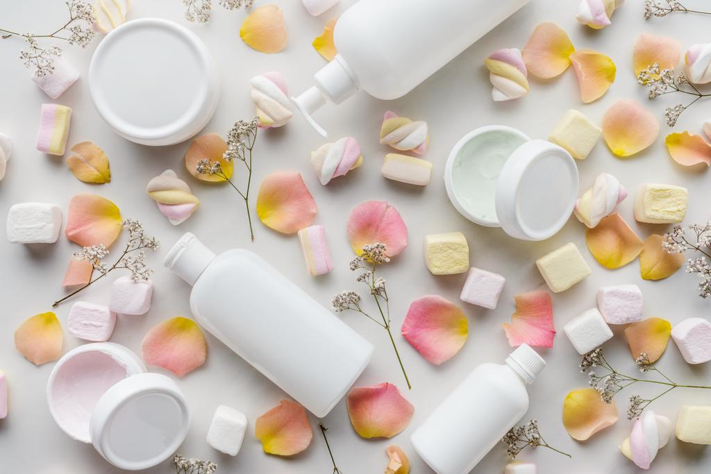 top view of bottles of cream, rose petals and marshmallows on white tabletop, beauty concept - Photo, Image