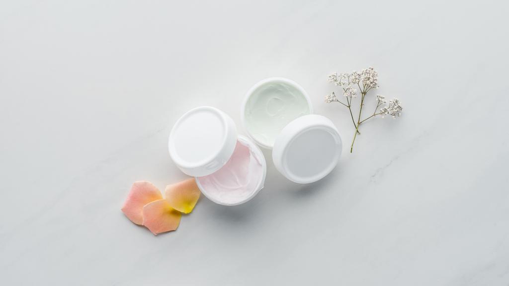 vista superior de botellas de crema, flores secas y pétalos de rosa en la superficie blanca, concepto de belleza
 - Foto, Imagen