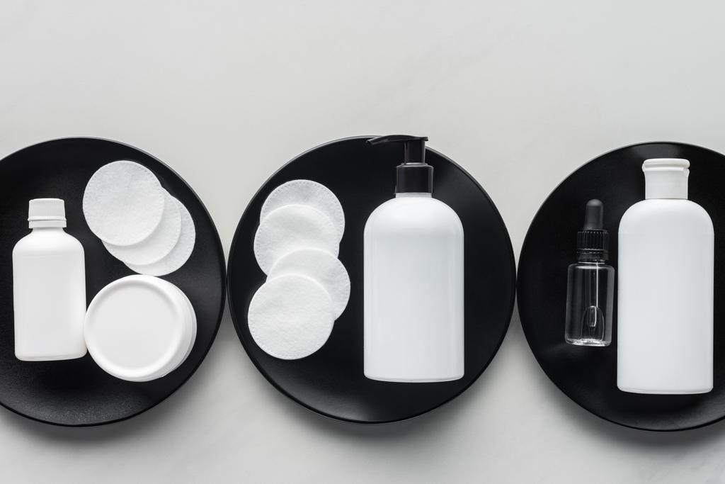 Draufsicht auf Cremeflaschen und Kosmetikkissen auf drei schwarzen Tellern, Schönheitskonzept - Foto, Bild