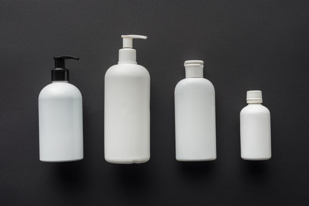κάτοψη του τέσσερα μπουκάλια λευκό κρέμα που απομονώνονται σε μαύρο, έννοια της ομορφιάς - Φωτογραφία, εικόνα