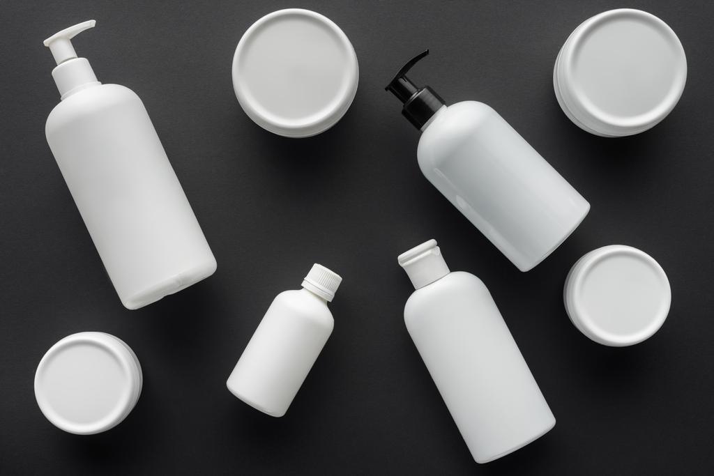 vista superior de botellas blancas dispersas de crema aisladas en negro, concepto de belleza
 - Foto, Imagen