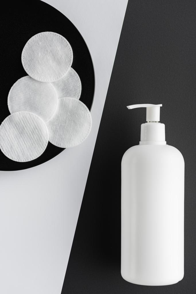 bovenaanzicht van fles crème en katoen pads op zwart-wit oppervlak, beauty concept - Foto, afbeelding